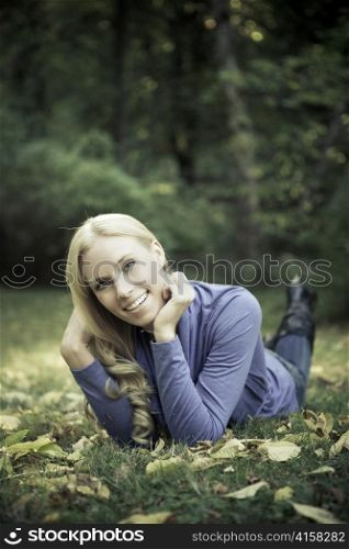 A portrait of a happy beautiful caucasian woman lying down on autumn leaves on the ground