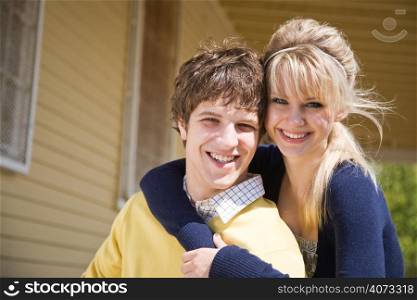 A portrait of a happy young caucasian couple in front of their house