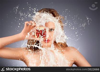 A portrait of a nude hot model with a pomegranate&acute;s half in her hand in milky splash.