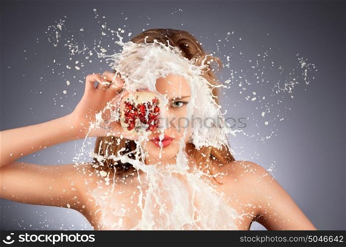A portrait of a nude hot model with a pomegranate's half in her hand in milky splash.