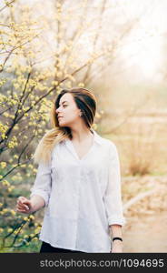 A portrait of a pretty long haired young woman in a garden enjoying blooming trees with yellow flowers, romantically looking to the side, film grain effect