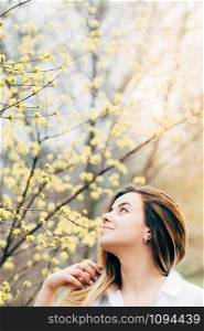 A portrait of a pretty young girl in a garden enjoying blooming trees with yellow flowers, romantically looking up, film grain effect