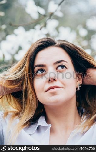 A portrait of a pretty young girl in a garden enjoying blooming trees with white flowers, romantically looking up, closeup view, blurred background