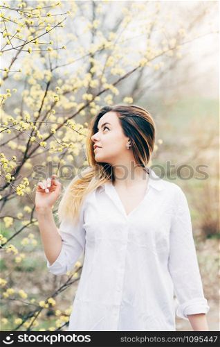 A portrait of a pretty young long haired woman in a garden, enjoying blooming trees with yellow flowers, romantically looking up, film grain effect