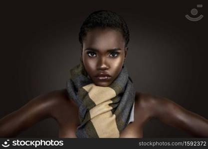 A portrait of a sensual young black female with short black hair, beautiful makeup and moist lips wearing a colorful scarf in front of a dark background.