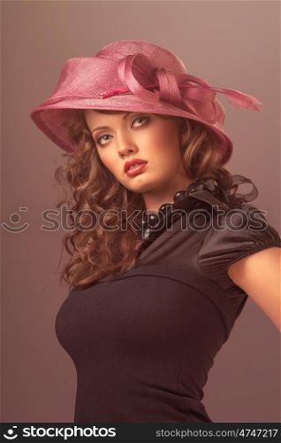 A portrait of a sexy brunette wearing a black retro dress and a rosy designer hat with a bow.
