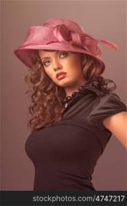 A portrait of a sexy brunette wearing a black retro dress and a rosy designer hat with a bow.