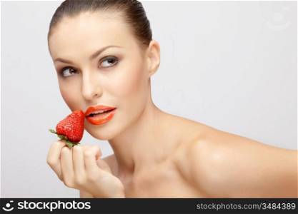 A portrait of a sexy lady holding a juicy strawberry near her lips.