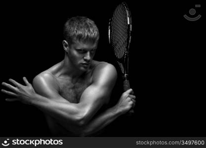 A portrait of a tanned sportive tennis player with a racket against black background.
