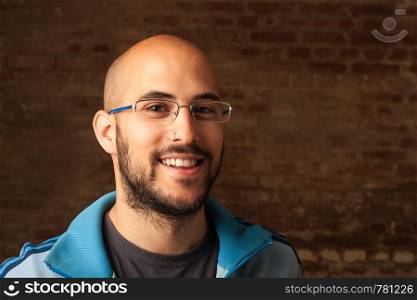 A portrait of a young bald man with a beard and glasses