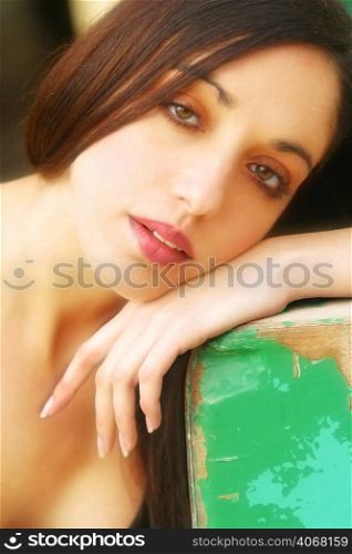 A portrait of an attractive woman leaning on a green piece of wood.
