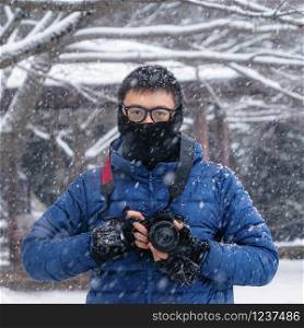 A portrait of Asian photographer holding a camera, looking at camera with white snow in winter, Japan in adventure concept during travel trip, vacation, or holidays. Nature background.