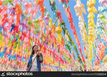 A portrait of Asian woman with colorful lanterns or lamps during travel trip and holidays vacation concept. Traditional festival in Harikulchai Temple, Lamphun, Thailand. Ceremony in Asia. Celebration