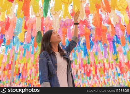 A portrait of Asian woman with colorful lanterns or lamps during travel trip and holidays vacation concept. Traditional festival in Harikulchai Temple, Lamphun, Thailand. Ceremony in Asia. Celebration