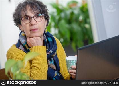 a portrait of beautiful brunette mature woman with a laptop at home