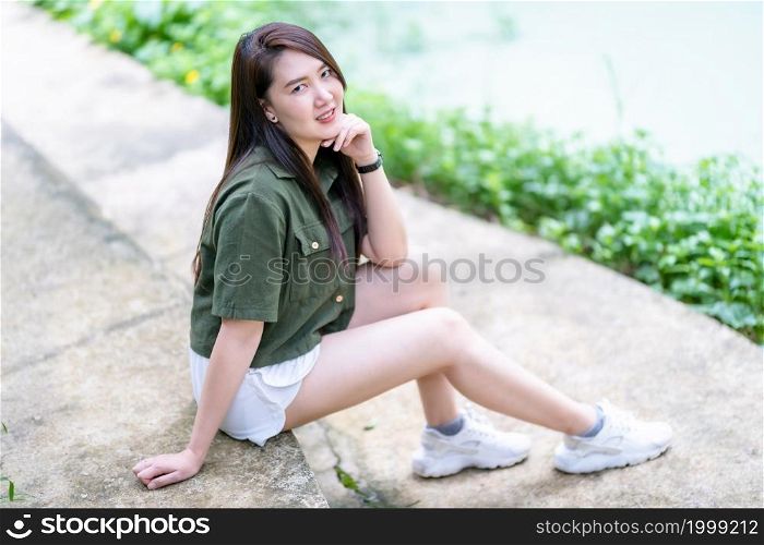 a portrait of beautiful happy asian woman traveler wearing brownish green dress stylish hipster Summer sunny lifestyle on the street outdoors at sunny summer day in park background