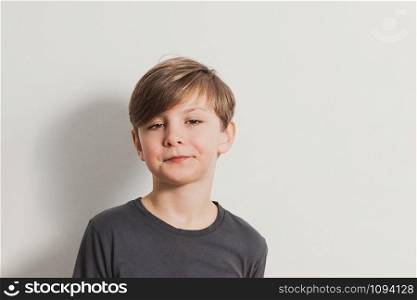 a portrait of cute boy pulling faces, snooty look, dark grey shirt, white wall. Copy space for your text and design