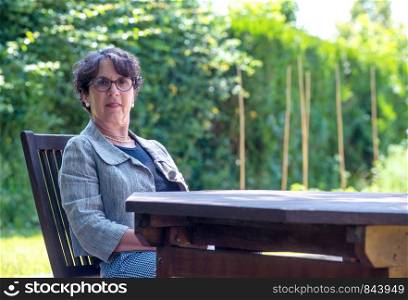 a portrait of senior woman with glasses sitting in the garden