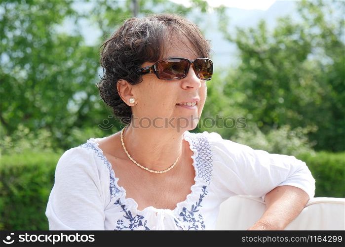 a portrait of smiling middle age woman sitting in garden at home