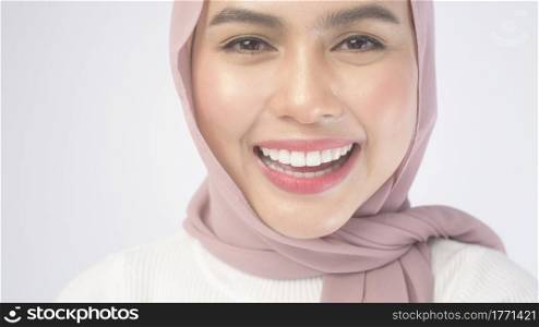 A portrait of young smiling muslim woman wearing a pink hijab over white background studio.. Portrait of young smiling muslim woman wearing a pink hijab over white background studio.