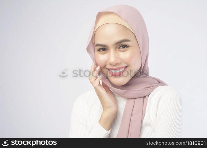 A portrait of young smiling muslim woman wearing a pink hijab over white background studio.. Portrait of young smiling muslim woman wearing a pink hijab over white background studio.