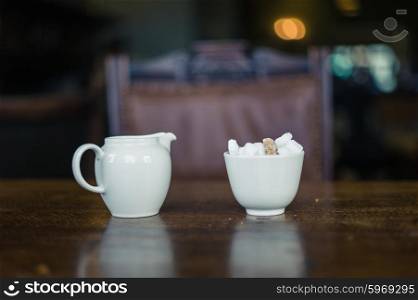 A pot of milk and a bowl of sugar cubes on a dinner table in a dining room
