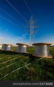 A power line tower in the field and bobbins with aluminum wire ready to installation