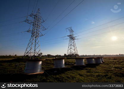 A power line tower in the field and six bobbins with aluminum wire ready to installation