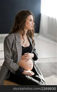 A pregnant girl with a bare stomach is sitting on a stepladder.. A photo of a beautiful pregnant woman with a bare stomach 4127.