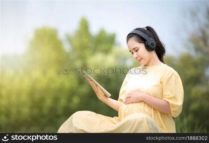 A pregnant woman is relaxing in the park and listening to music on a tablet, Mom listening Songs for the unborn child, Pregnant near giving birth, mother and child