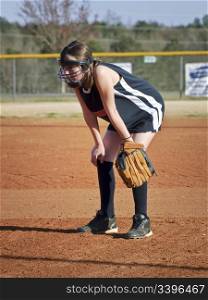 A preteen girl playing her position during a softball game with her safety eauipment on.