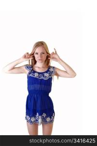 A pretty and slim young woman standing in her blue short dress and long blond hair, with her fingers in her ears for white background in the studio.
