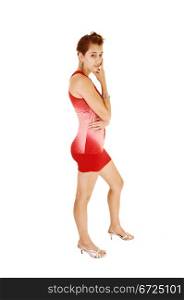A pretty and young woman from the side in a red short and tight dressstanding in high heels for white background with her lovely figure.