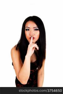 A pretty Asian woman in a red and black dress standing for white backgroundwith her finger over her mouth, be quiet.