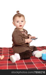 A pretty baby girl in a brown dress sitting on a blanket on the floor,isolated for white background.