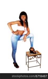 A pretty black woman in blue tights and long black hair standing for whitebackground having one leg on a small bench.