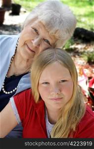 A pretty blond girl and her grandmother in the garden. The little girl looks serious. Vertical view.