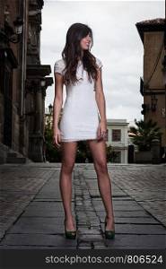 A pretty brunette girl with white dress in the middle of the street