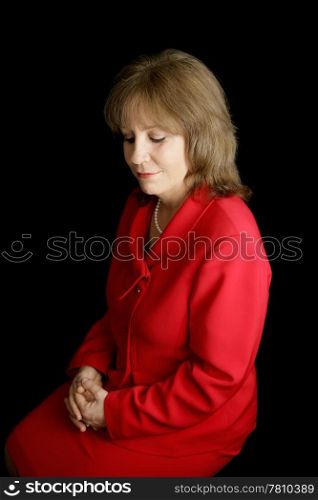 A pretty business woman in a red suit, alone with her thoughts. Black background.