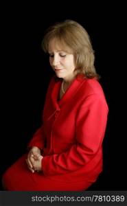 A pretty business woman in a red suit, alone with her thoughts. Black background.