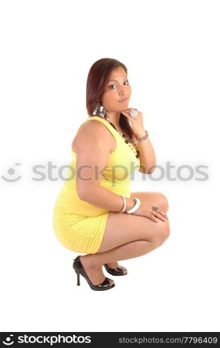 A pretty full figured young woman in a yellow dress and high heels and necklace crouching on the floor with her red hair for white background.