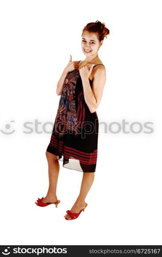 A pretty girl in a black colorful dress and high heels standing for whitebackground holding her thumps up for good luck.