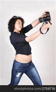 A pretty Hispanic woman try to take a picture of herselfin a black blouse and jeans, over light gray.