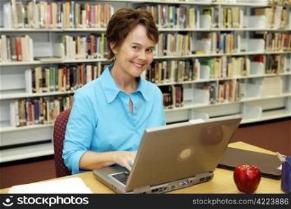 A pretty librarian working on her laptop computer in the school library.