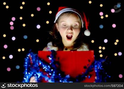a pretty little girl opens her Christmas present on black background