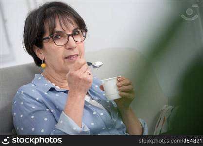 a pretty mature woman eating a yogurt at home