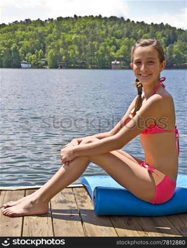 A pretty preteen girl posing on a dock at the lake.