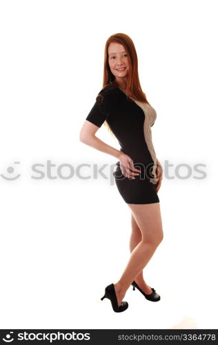 A pretty red haired woman in a black gray dress standing in the studio,looking into the camera, on white background.