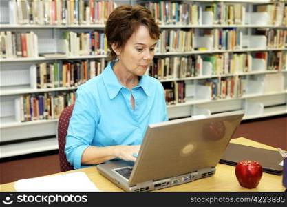 A pretty school librarian doing researh online in the media center.