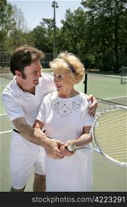A pretty senior woman getting a tennis lesson from a handsome young pro.